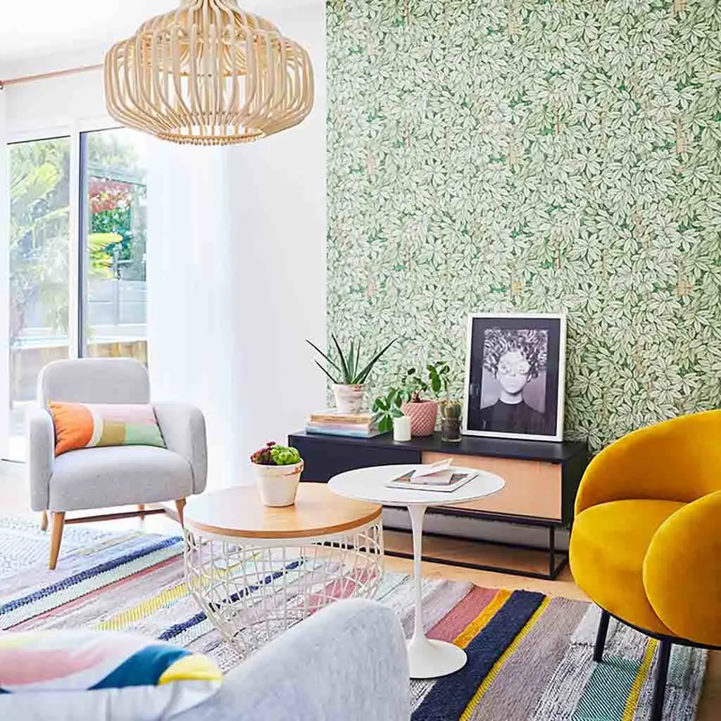 Salon décoré avec des fauteuils en tussus, une suspension en bois et un papier peint feuillage